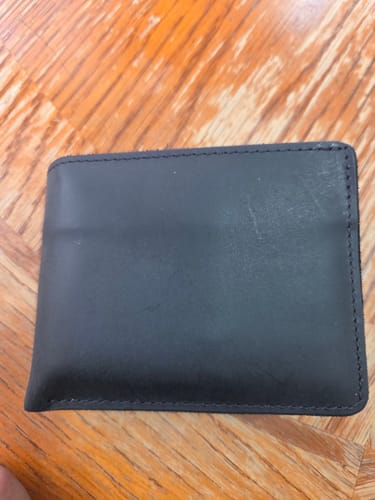 Customer's black Huron Premium Bifold wallet closed and lying on a wooden table.
