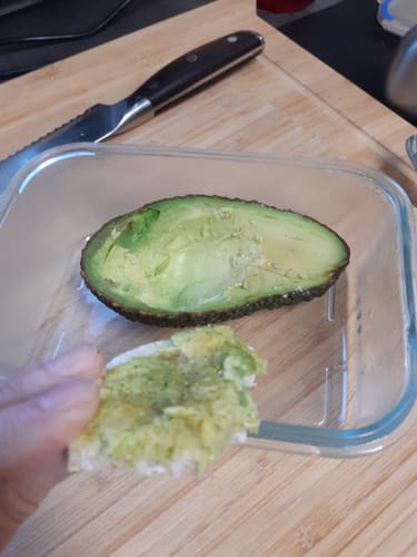 Ein Kunde zeigt eine halbierte, ausgehöhlte Bio Hass Avocado und ein Stück Brot mit dem Aufstrich.