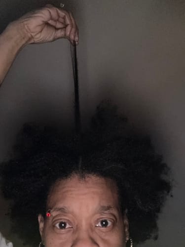 Customer holding up a single strand of their thick, dark hair to show its length after using the Scalp Stimulator.