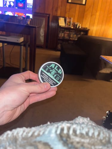 Customer holding the round, silver tin of Refreshing Chill Nicotine Pouches in their living room.