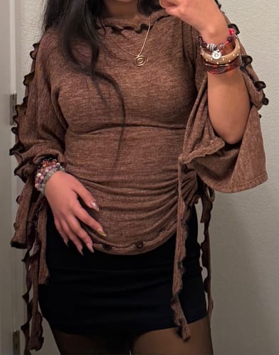 Una clienta viste el suéter She Shell en color marrón jaspeado sobre una falda negra, mostrando las mangas con volantes.