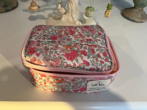 Customer's pink floral Sanrio cosmetic bag sitting on a white table with the top compartment partially unzipped.