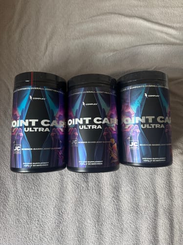 Customer's three black tubs of Complex Joint Care Ultra supplement arranged side-by-side on a bed.