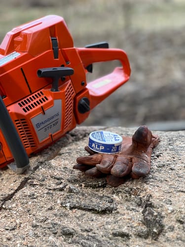 Customer's can of Chilled Mint Nicotine Pouches resting on a leather glove next to a chainsaw outdoors.