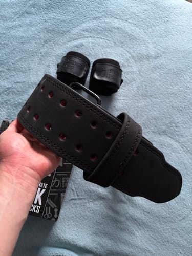 Customer's hand holding a new black lifting belt with the Stealth Black Wrist Wraps resting on a towel.