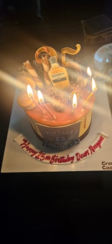 Reviewer's Chocolate and Whiskey cake customized for a 25th birthday with lit candles and a whiskey bottle topper.