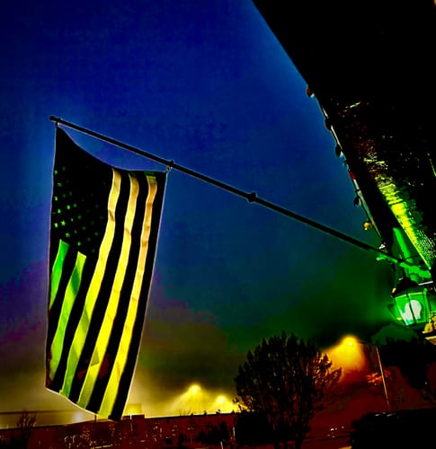 Reviewer's heavy duty American flag hanging from a pole outdoors at night, illuminated by a light.