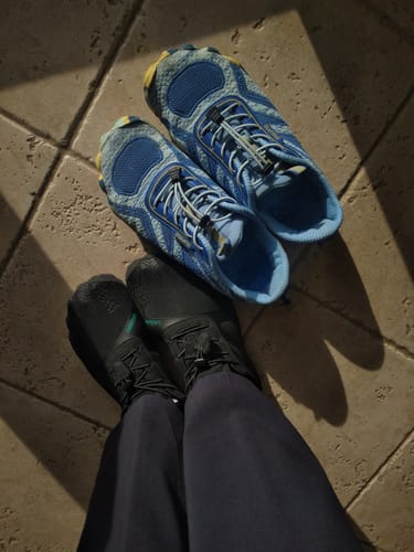 Customer sits wearing black Vitality III shoes, with their new blue pair placed on the floor beside them.