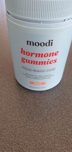 Reviewer's close-up of the light blue tub of peach-flavored Hormone Gummies on a table.