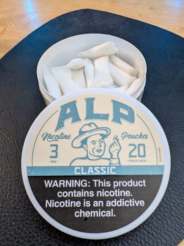 Customer's open tin of ALP Classic Nicotine Pouches showing the loose, dry pouches inside with the lid resting against it.