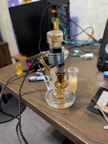 Customer's multifunction Mystery Dab Rig in clear and amber glass sitting on a desk.