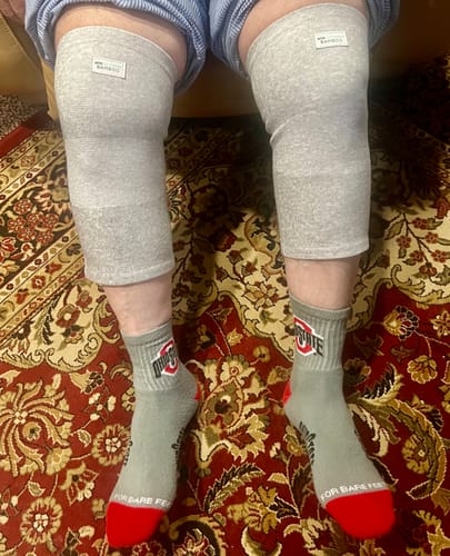 Customer sitting down while wearing a pair of light grey Premium Bamboo Knee Sleeves on both knees.