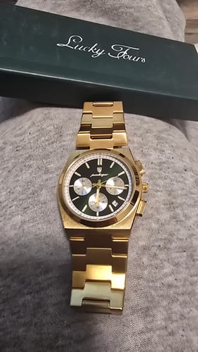 Reviewer's gold-tone Lucky Fours® Prague watch with a dark green face, shown with its box on a grey surface.