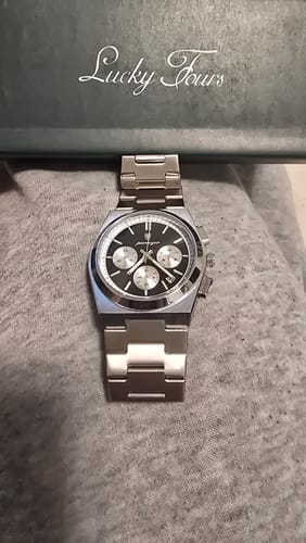 Reviewer's silver Lucky Fours® Prague watch with a black dial, shown on a surface with its box in the background.