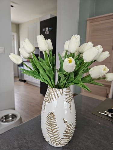 Recensent toont het boeket witte tulpen in een decoratieve vaas op een aanrecht.