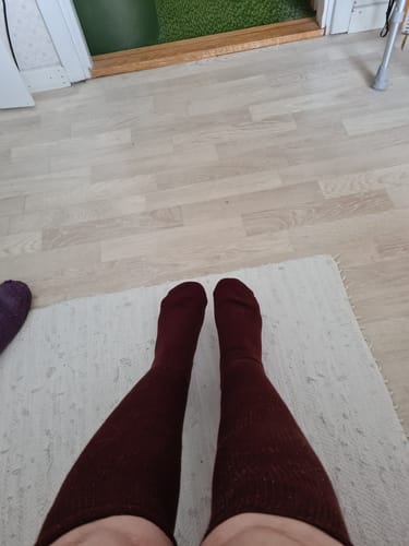 En kunds fötter och ben i mörkröda Diasocks Komfortstrumpor, sedda uppifrån.