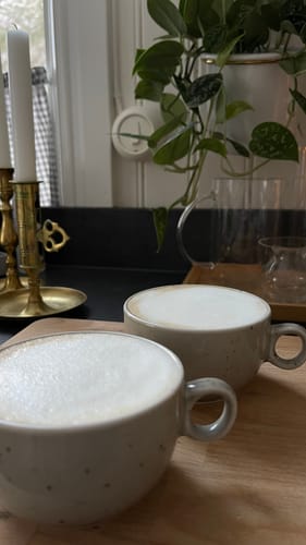 Kundens två prickiga Dotty Kaffekoppar fyllda med kaffe, ståendes på en träbricka.