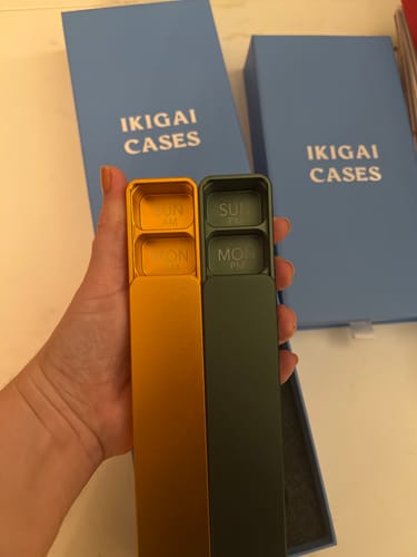 Customer holds two open Weekly AM-PM Pill Cases 2.0, one yellow and one green, showing the inner compartments.