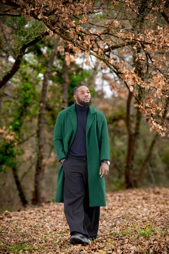 Reviewer standing in a forest wearing the green woolen over-the-knee coat over black clothing.