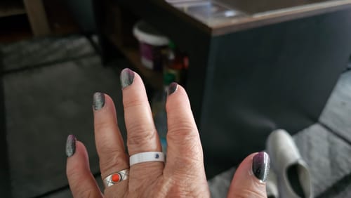 Kundin zeigt ihre dunklen, glitzernden UV-Gelnägel nach einer Woche.