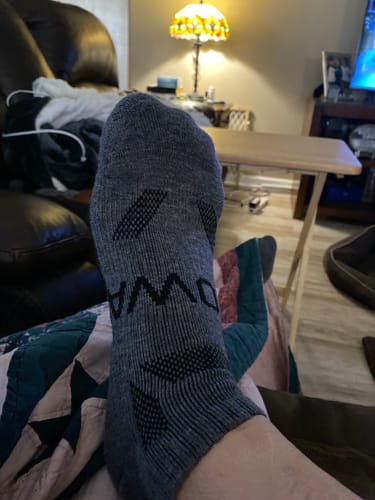 Customer relaxing with their foot up, wearing a grey Men's Alpaca Sock with black patterned details.