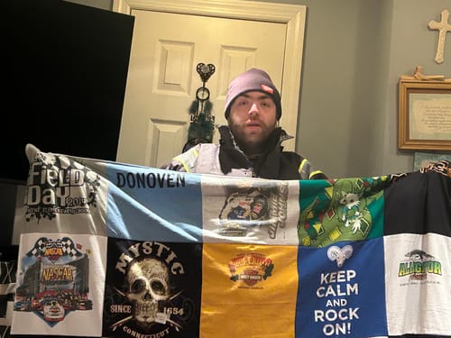 A person holding up their new Premium T Shirt Quilt, showing a collage of colorful graphic squares.