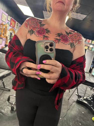 Customer displays colorful floral tattoos on their chest and shoulders, with calm skin after using the numbing cream.