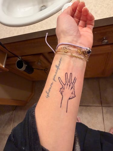 A reviewer's forearm with a custom sketch-style temporary tattoo of two overlapping hands.
