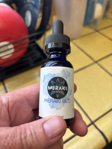 Customer's hand holding a blue dropper bottle of Meraki Blu.
