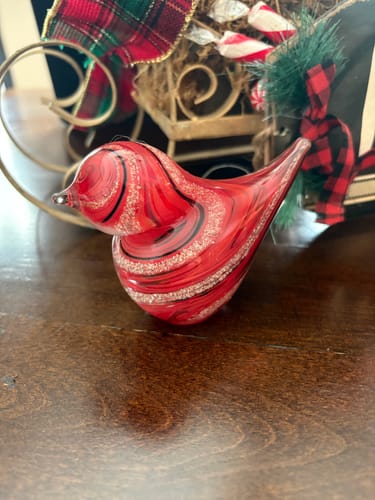 Customer's red glass bird with cremation ash, featuring a swirled design, on a wooden surface.