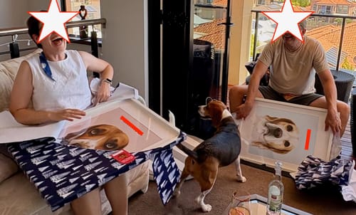 Customers laughing as they unwrap two framed Custom Pet Portraits, with their beagle standing between them.