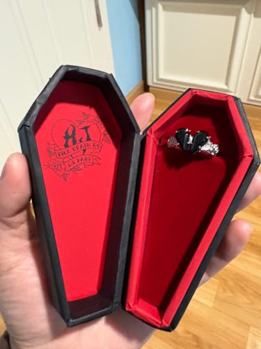 Reviewer holding the PROMISE RING in its open, coffin-shaped black box with a red interior.
