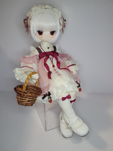 Reviewer's 'Petite Strawberry - Meira' doll sitting on a stand, wearing a frilly dress and holding a small basket.