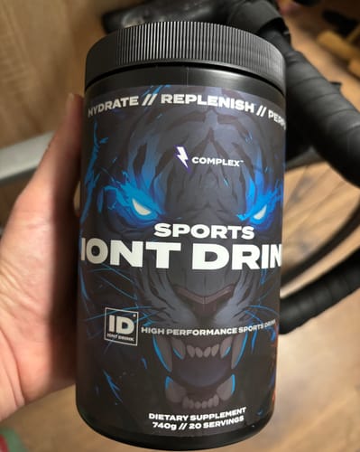 Customer holding a black tub of Complex Sports Iont Drink with a striking blue tiger graphic on the label.