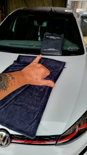 Reviewer's hand over the dark BLACKLINEĀ® drying towel spread on the hood of a white car.