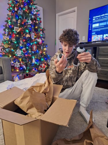 A person unboxing the BLACKLINEĀ® BOX by a Christmas tree, holding and looking at two car detailing products.