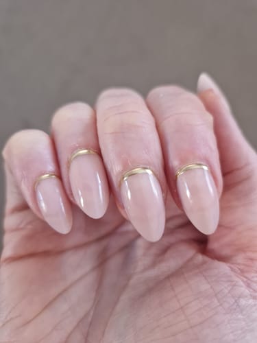 Reviewer's hand showing the Golden Crescent press-on nails after one week of wear, with a neat almond shape and gold cuticle accent.