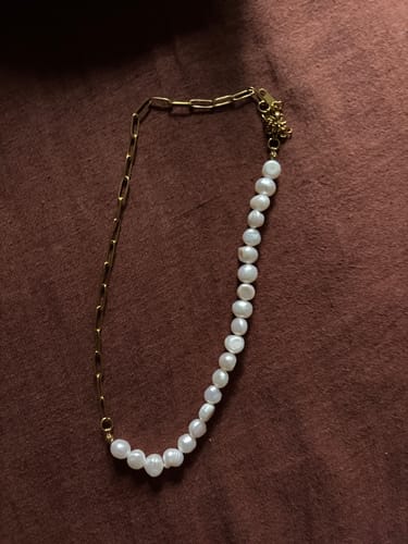 Reviewer's Rhoni necklace laid on a brown surface, showing its half gold paperclip chain and half pearl design.