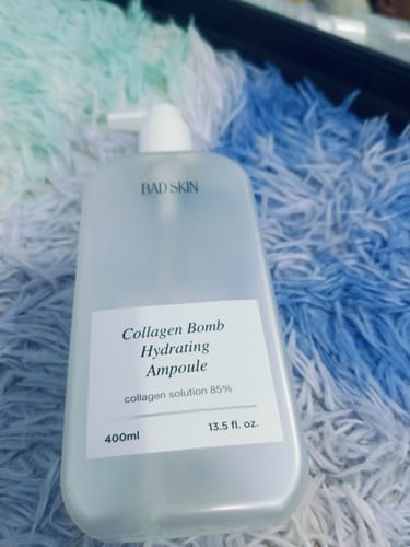 Customer's large bottle of Bad Skin Collagen Bomb Hydrating Ampoule on a fluffy, multicolored surface.