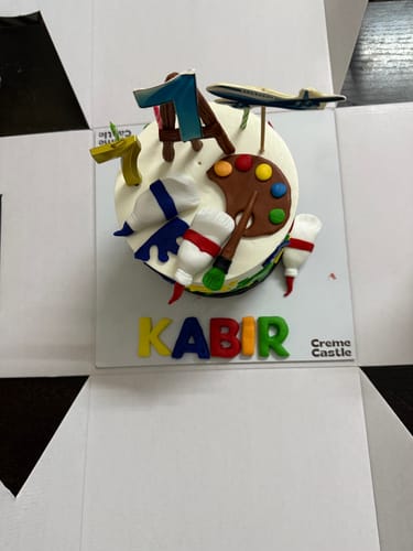 Customer's customized Painter's Delight Cake with an artist theme, the number 1, a model airplane, and the name 'Kabir'.