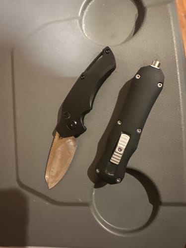 Customer's Grunt Automatic Switchblade Knife with blade deployed, shown next to their black OTF knife on a gray surface.