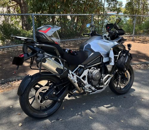 Reviewer's black Wind Rider Seat Cover fitted snugly on their silver motorcycle, parked outdoors.
