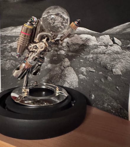 Customer's assembled Nebula Astronaut figurine with shiny, metallic parts on a black base, set against a moon-themed backdrop.