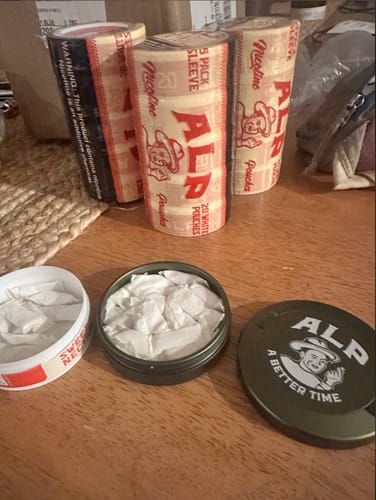 Reviewer's sleeves of Sweet Nectar Nicotine Pouches and two open tins showing the white pouches on a table.