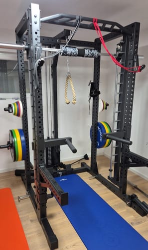 Rezensent zeigt sein schwarzes R7-Daemon Power Rack in einem Heimstudio, wobei die Multipresse für mehr Platz hinten montiert ist.