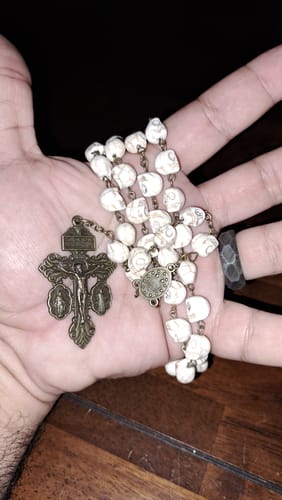 Customer's hand holding the Saint Benedict Skull Rosary, showing the white beads and detailed crucifix.