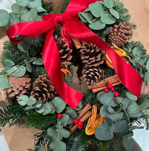Customer's festive wreath from the workshop, showing a large red bow, pine cones, and dried oranges.