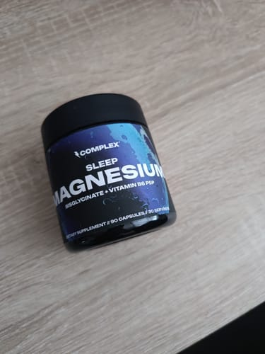 Reviewer's black jar of Complex Sleep Magnesium supplement resting on a wooden table.