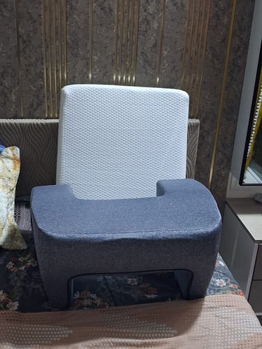 Reviewer's grey Frido Ultimate Wedge Plus Cushion positioned on a bed in front of a white backrest.