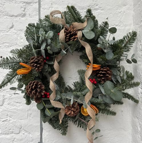 Customer's finished wreath from the workshop, decorated with pine cones, eucalyptus, dried oranges, and a rustic burlap ribbon.